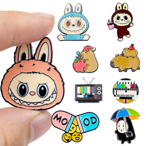 Hand holding cute anime character badges including pink rabbit, black robot, and small penguin
